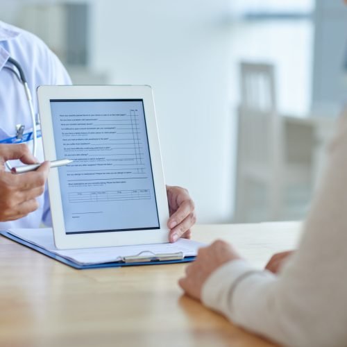 Close-up shot of physician pointing at screen of digital tablet, female patient listening to him with concentration